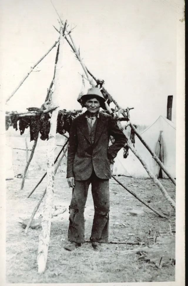 Man beside a meat drying rack at camp